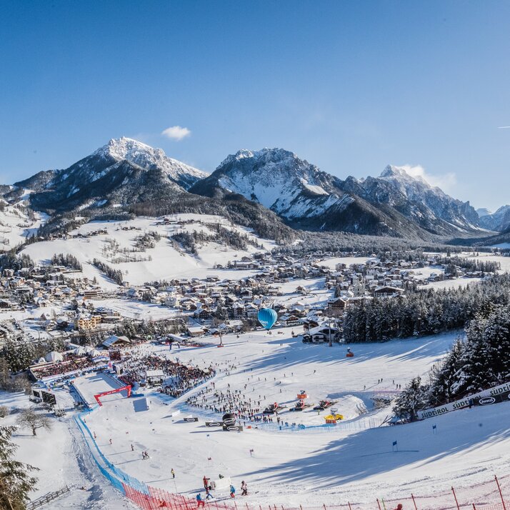 Skirennstrecke und Ortschaft im Vordergrund und blauer Himmel, verschneite Wälder und Berge im Hintergrund. | © Harald Wisthaler