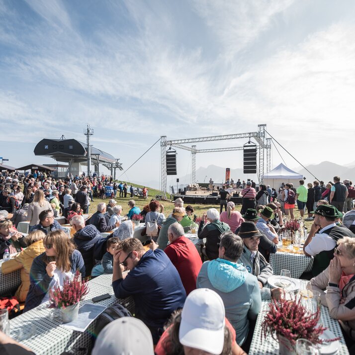 Zahlreiche Menschen sitzen an langen Tischen vor einer Bühne bei einer Freiluftveranstaltung. | © Gianvito Coco