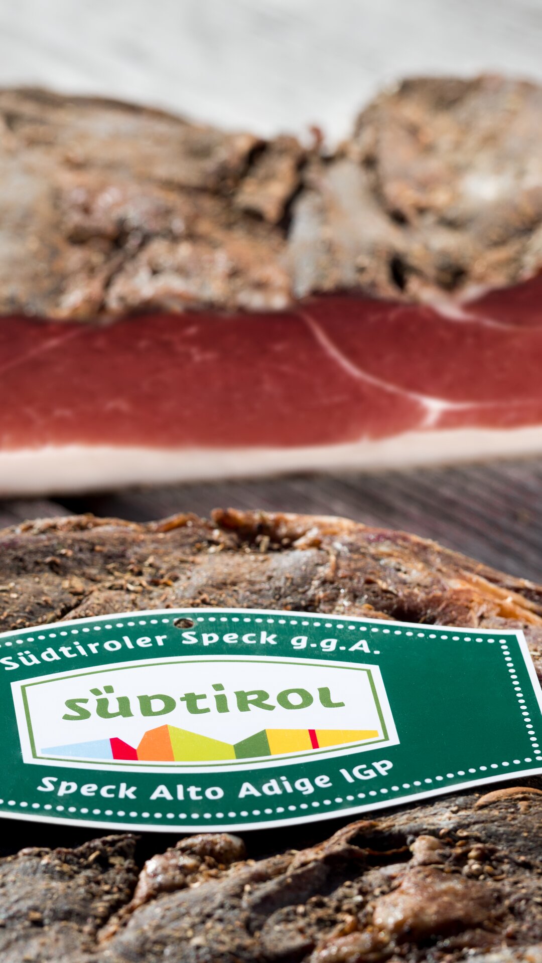 Zwei Speckseiten von originalem Südtiroler Speck auf einem Holztisch. | © Helmuth Rier