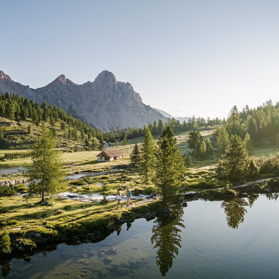 Der stille Bergsee spiegelt Nadelbäume und eine gezackte Bergkette bei klarem Morgenlicht. | © Harald Wisthaler