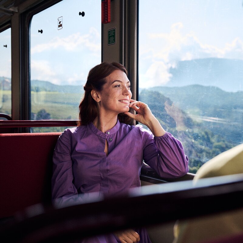 Die Frau sitzt entspannt im Zug und blickt aus dem Fenster in die Berglandschaft. | © IDM Südtirol