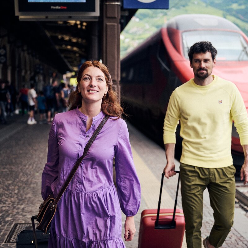 Eine Frau und ein Mann mit Koffern gehen an einem roten Zug entlang. | © IDM Südtirol