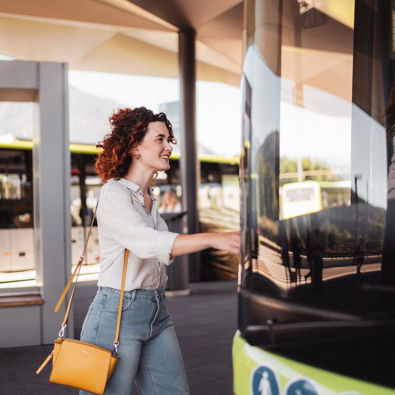 Eine Frau mit Sonnenbrille steigt mit einem Lächeln in einen gelb-schwarzen Linienbus. | © IDM Südtirol