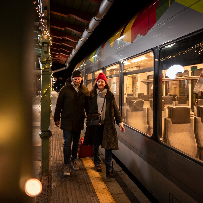 Weihnachtliches Flair am Bahnhof mit einem Paar das mit Koffern aus dem Zug aussteigt.