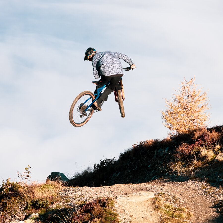 Ein Mountainbiker performt einen Sprung auf einem Bergweg. | © Daniel Niederkofler