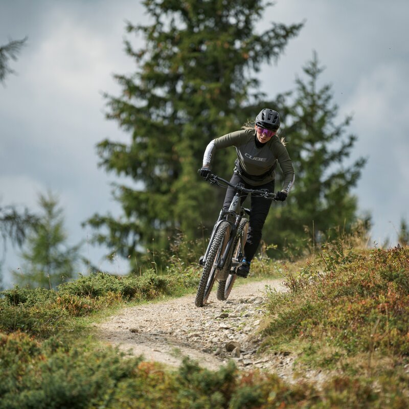 Ein Mountainbiker fährt konzentriert auf einem schmalen Waldrand-Trail bergab. | © Cube Bikes