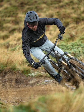 Ein Mountainbiker legt sich kraftvoll in eine Kurve auf einem schmalen Trail durch herbstlich trockenes Wiesengelände. | © Cube Bikes