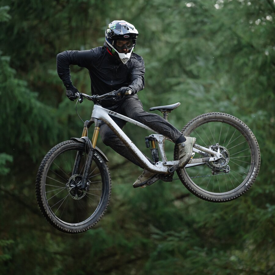 Ein Mountainbiker springt mit einem Trick in der Luft durch einen Waldabschnitt, das Rad seitlich gedreht, der Blick nach unten gerichtet. | © Cube Bikes