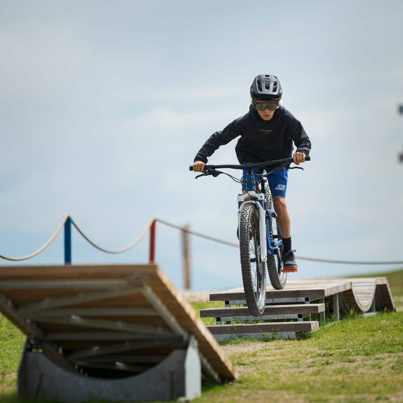 Ein Kind fährt mit dem Fahrrad über eine kleine Holzwippe auf einer Übungsstrecke im Freien. | © Cube