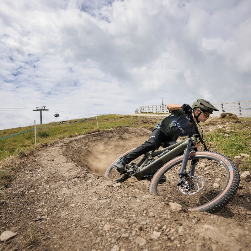 Ein Mountainbiker fährt eine steile, steinige Kurve hinunter, im Hintergrund eine Gondelbahn. | © Cube