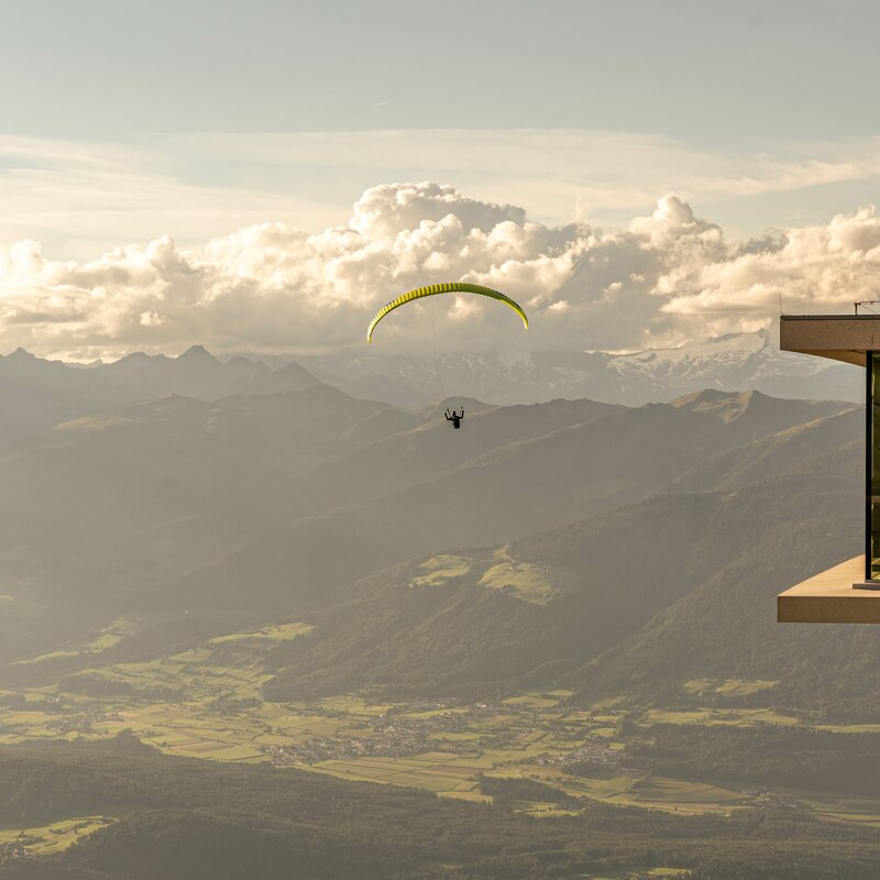 Ein Paragleiter fliegt neben dem AlpiNN Restaurant bei Sonnenuntergang. | © Skirama Kronplatz