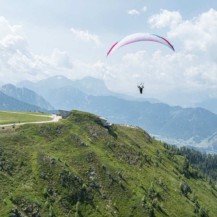 Ein Gleitschirmflieger schwebt über einer grünen Berglandschaft mit weitem Blick auf das Tal. | © Harald Wisthaler