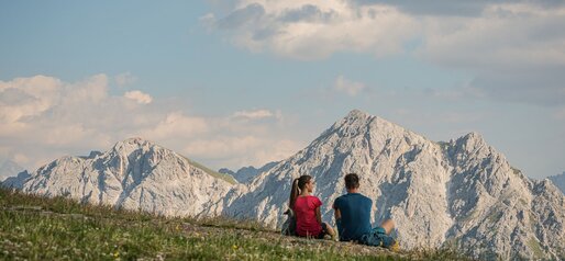 Ein Mann und eine Frau sitzen in der Wiese und schauen sich das Bergpanorama der Dolomiten an. | © Harald Wisthaler