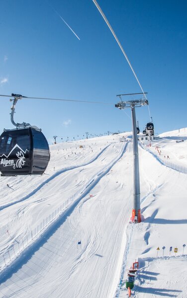 Eine Gondelbahn vor dem Hintergrund einer Skipiste und blauem Himmel.  | © Harald Wisthaler