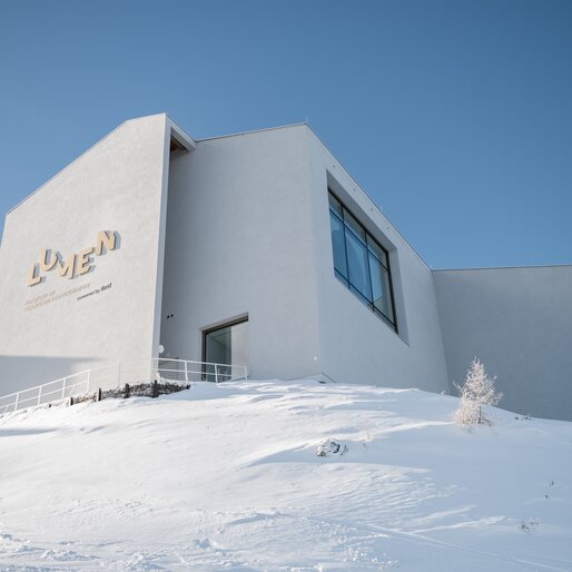 Die verschneite Außenfassade des LUMEN-Museums leuchtet in der Wintersonne vor tiefblauem Himmel. | © Gianvito Coco