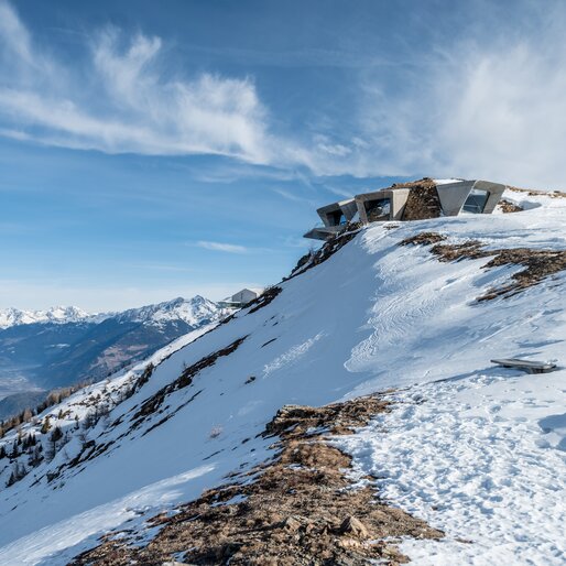 Ein modernes Gebäude thront auf einem leicht verschneiten Hügel empor. | © Gianvito Coco
