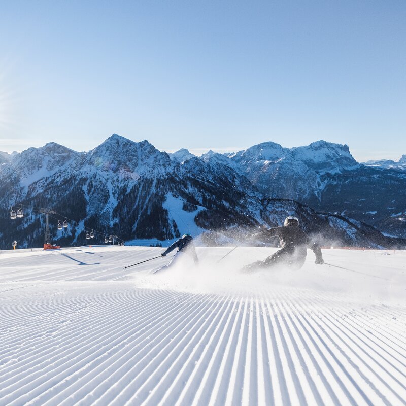 Zwei Skifahrer auf einer Piste bei strahlendem Sonnenschein in den Dolomiten. | © Harald Wisthaler