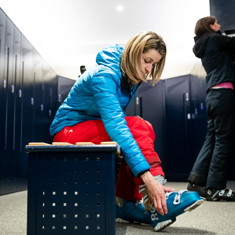 Eine Skifahrerin zieht sich im Depot ihre Skischuhe an. | © Skiarea Miara