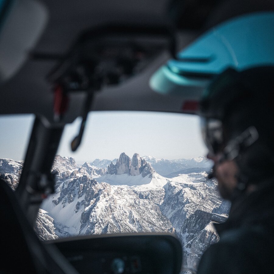 Der Blick aus einem Cockpit eines Helikopters in die Berglandschaft, im Vordergrund das Profil des Piloten. | © Kottersteger